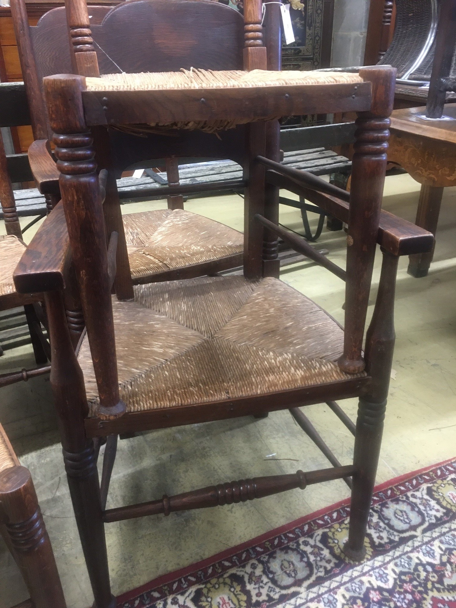 A set of six Arts & Crafts oak chairs, including a pair of carvers, in the Glasgow School manner by William Birch, High Wycombe, with shaped panels backs, ring turned frames and rush seats, carvers W.58cm D.54cm H.109cm